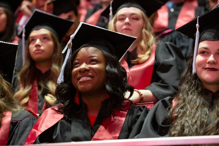 An IU graduate wearing a cap and gown smiles during commencement