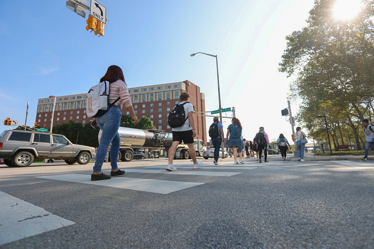 People wearing backpacks walk across the street at a crosswalk on a sunny day