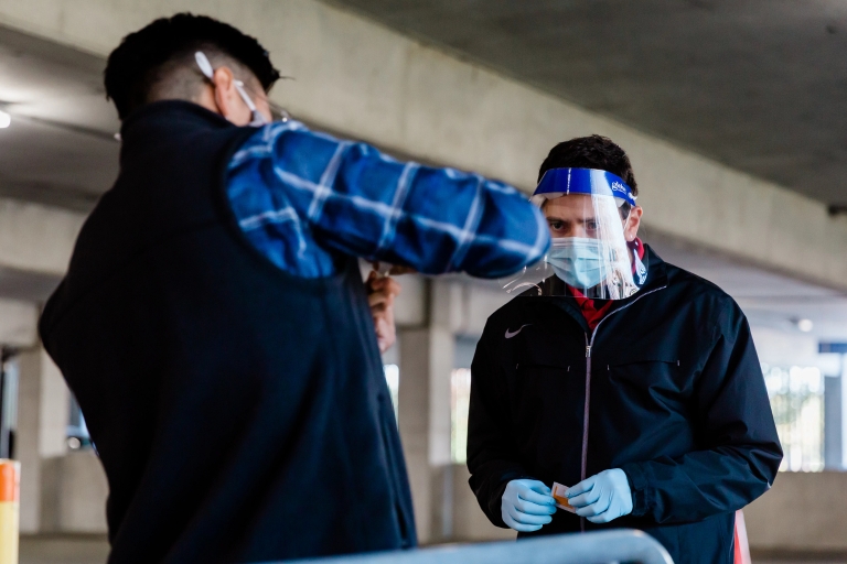 An IU testing site worker watches as a man submits his saliva sample for COVID-19 testing