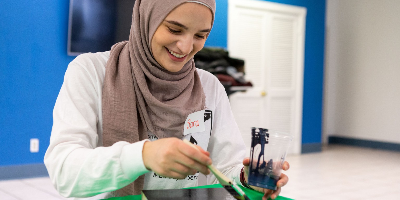A student wearing a head scarf paints wood decor