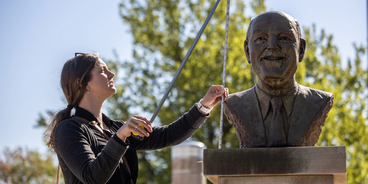 Sonja Rogers uses a tape measure to record the height of a bust of Bill Armstrong.