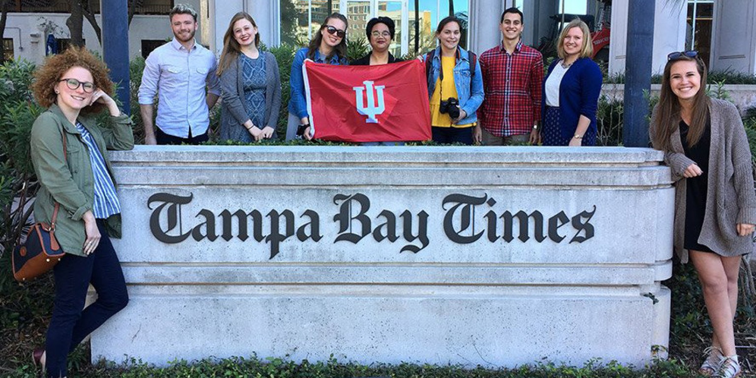 Students from The Media School standing in front of the Tampa Bay Times sign with the IU flag