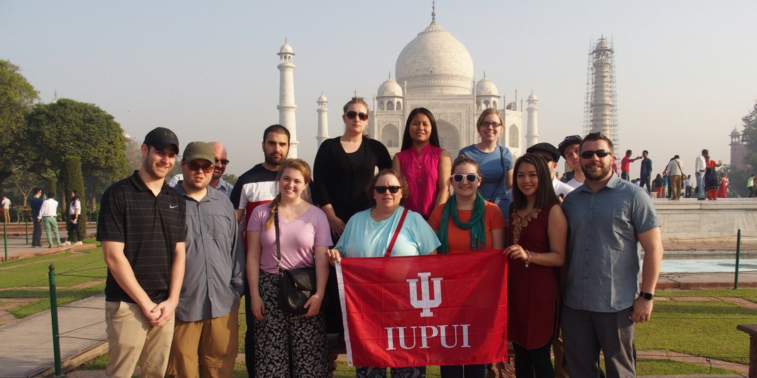 A group of people standing in front of the Taj Mahal in India holding an IU flag