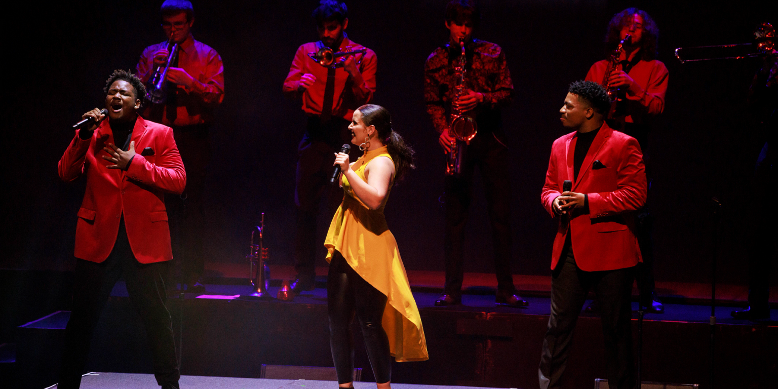 Three singers backed by a horn section perform on stage