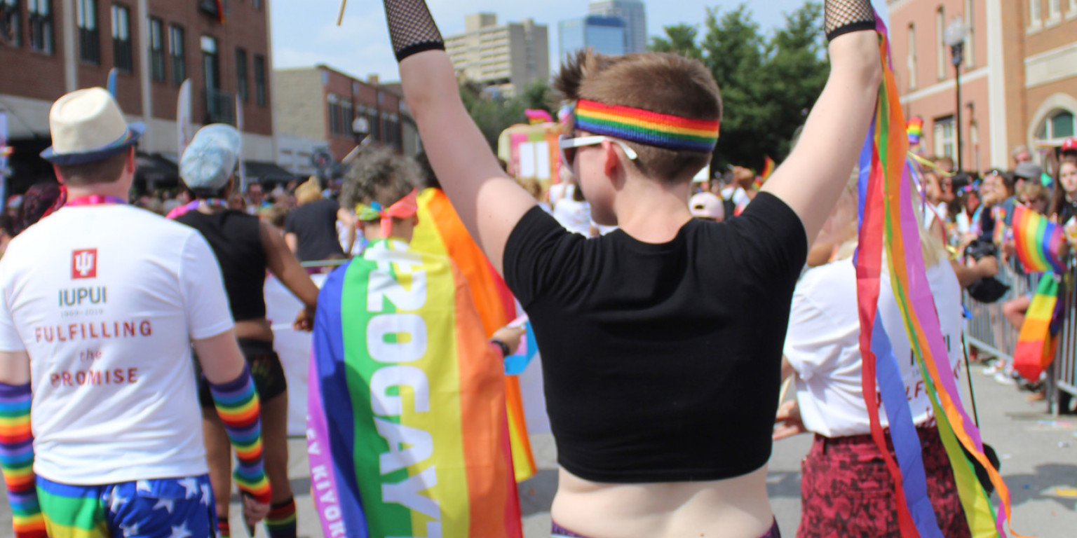 Person walks in 2019 Indy Pride parade waving the asexual pride flag and gay pride flag.