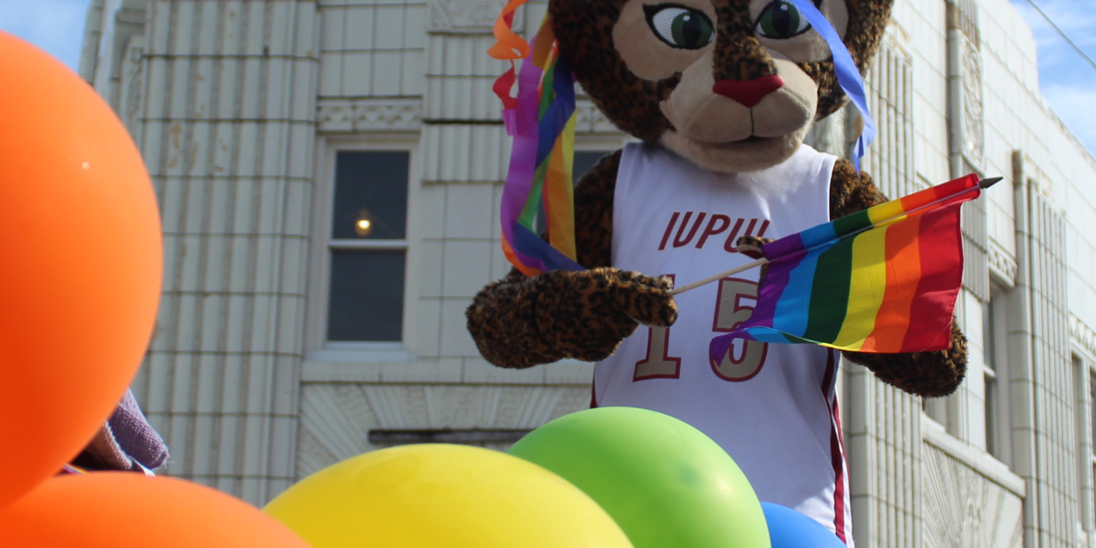Jazzy, an IUPUI Jaguar mascot, rides a float and waves a pride flag in the 2019 Indy Pride parade.