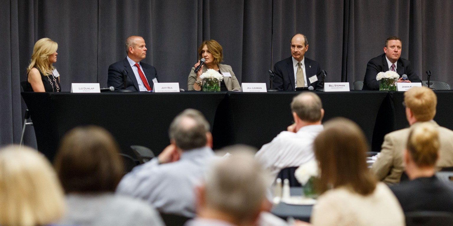 Panelists at the 2017 E2E Convergence sit at a long table, as Jill Lehman speaks into a microphone.