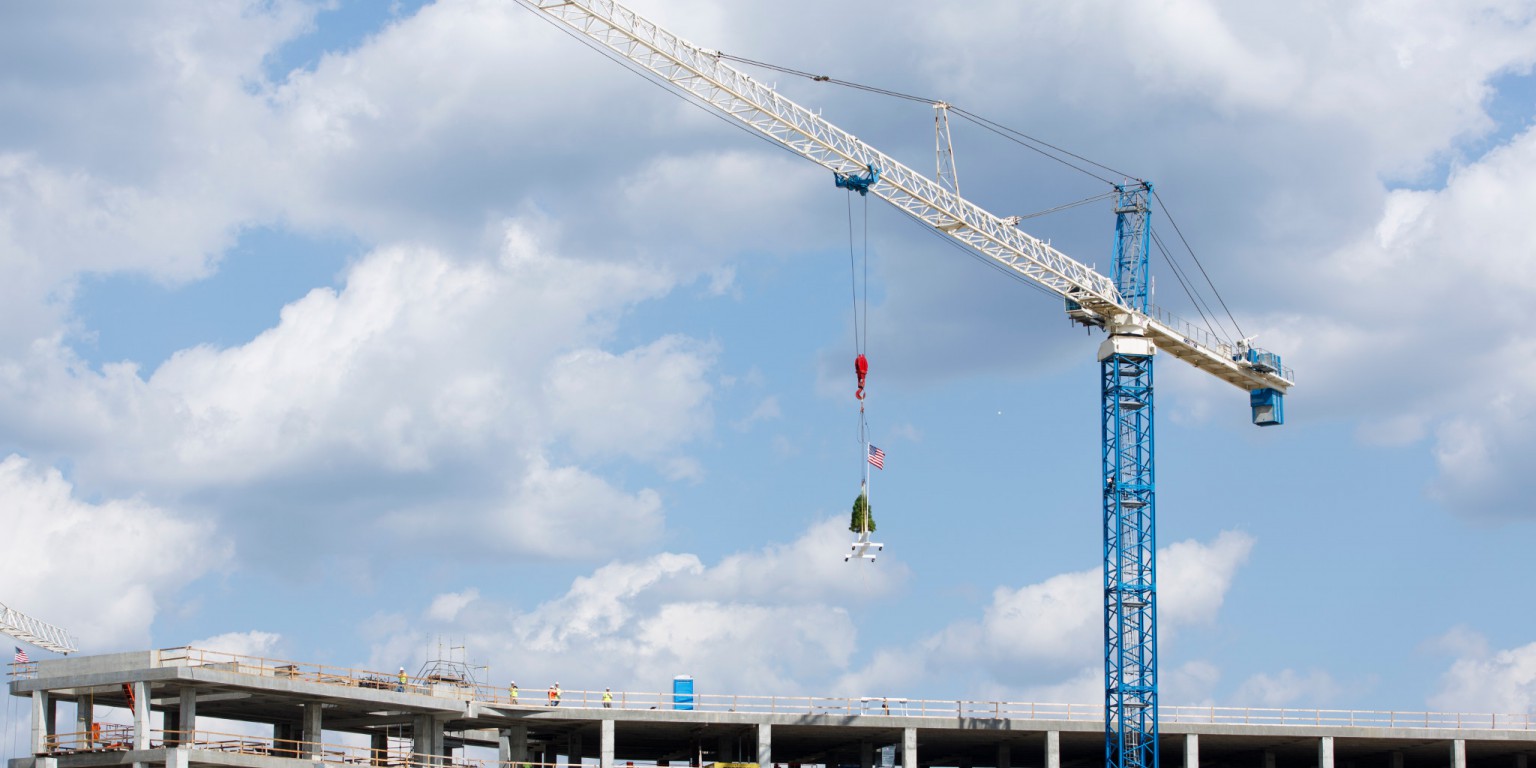 A crane lifts the final beam into place on top of the building