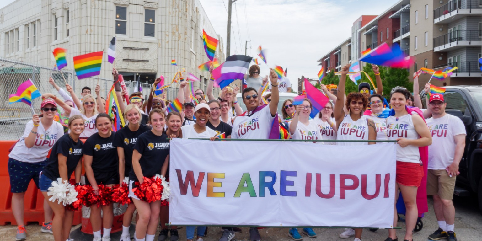 IUPUI students, faculty and staff hold a banner and wave pride flags during 2019 Indy Pride parade.