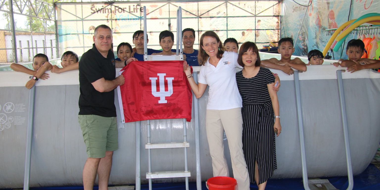 Bill Ramos and IU alum Beth Kreitl hold an IU flag at a pool in Vietnam.