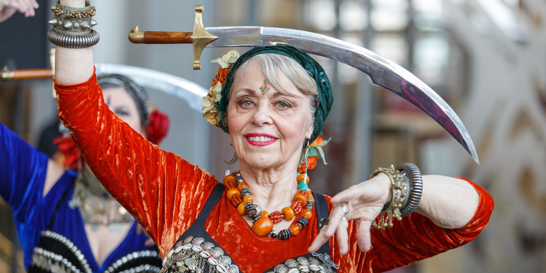 A woman in ethnic clothing dances with a curved sword balanced on her head.