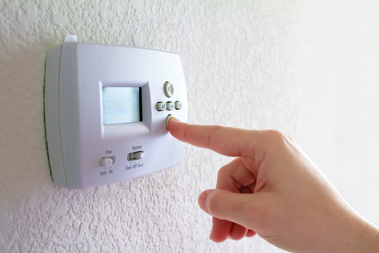 Person pressing a thermostat on the wall.