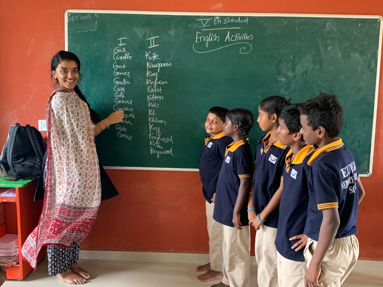 Nidhi Ramanathan stands at a blackboard with students lined up before her