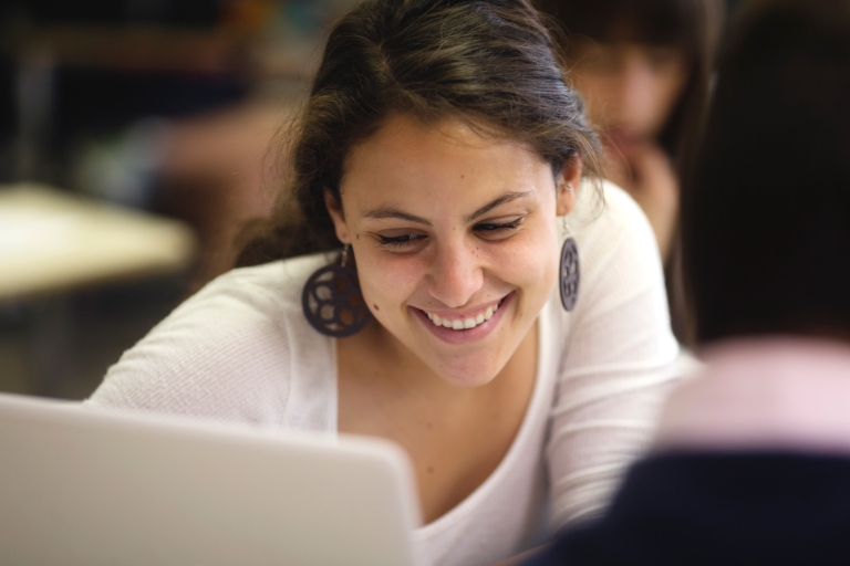A woman smiles at a computer screen.