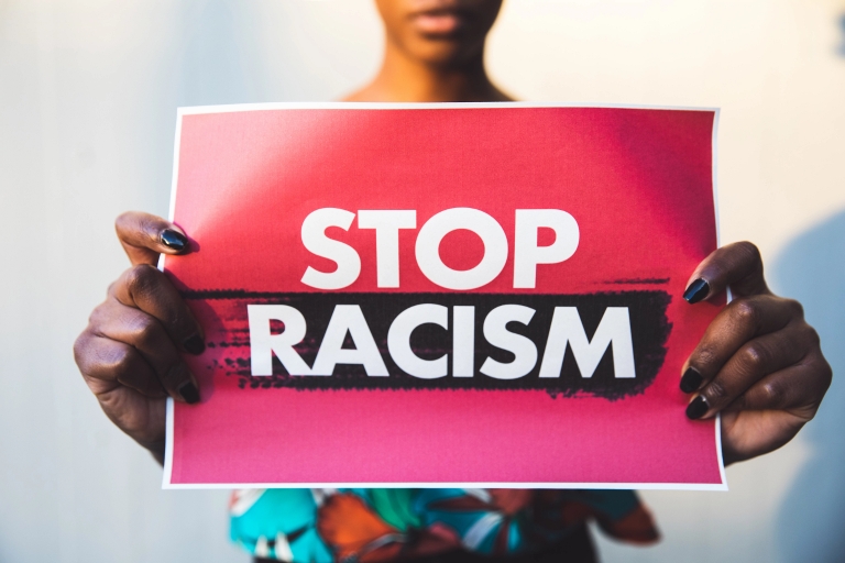 A Black woman holds a red sign with white lettering that says 