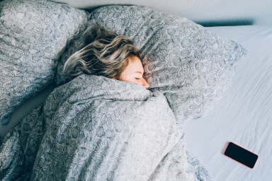 Woman sleeps in bed with covers pulled up over her mouth