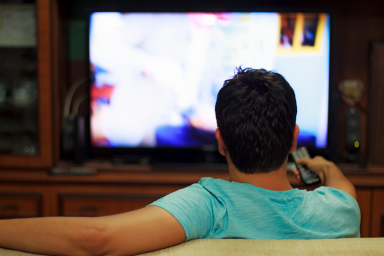 Man watches television with remote control in his hand
