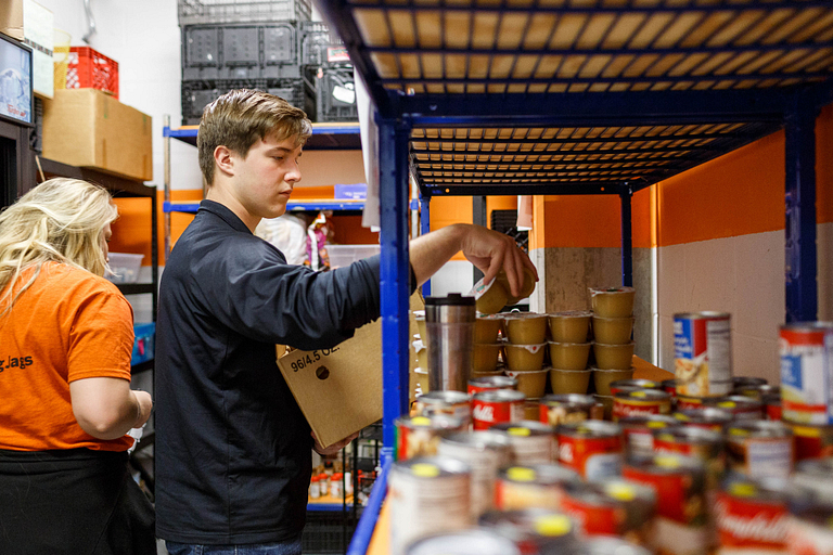 A student organizing canned items on shelves at Paw's Pantry