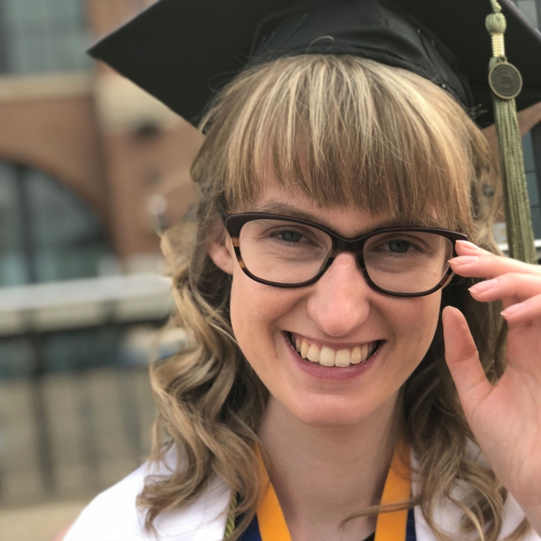 Ali Emswiller smiles at the camera, she is wearing a cap and gown for graduation