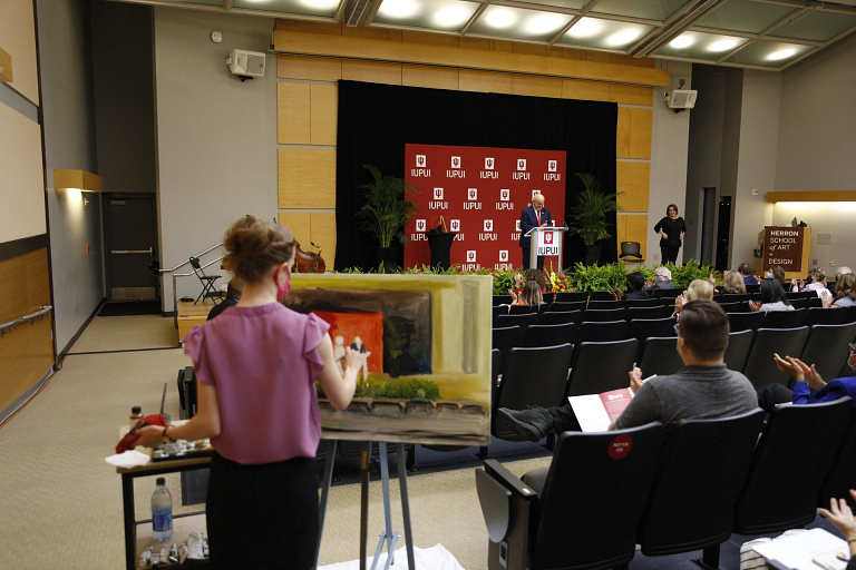 An artist paints a picture of the stage in the background in an auditorium.