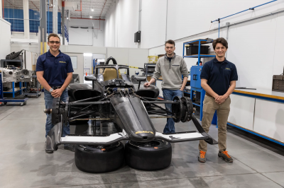 Alex Turner, Parker Neale and Max Grau stand around a race car at the Dallara IndyCar Factory