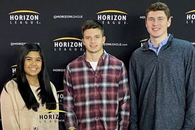 Sports management students stand around a table promoting the Horizon League Tournament