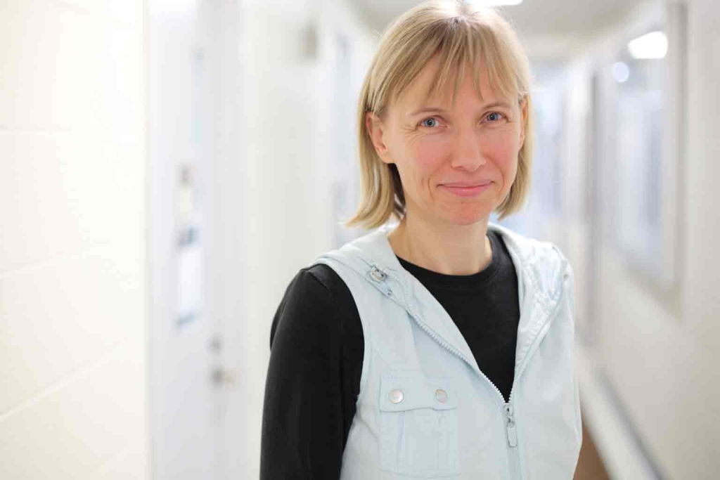 Katy Börner smiles at the camera, she is standing in a long white corridor
