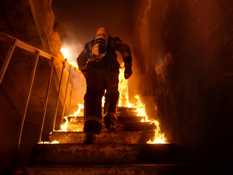 A firefighter running up a burning staircase