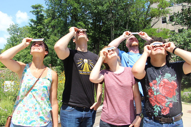 Students looking up at the sky through solar eclipse glasses