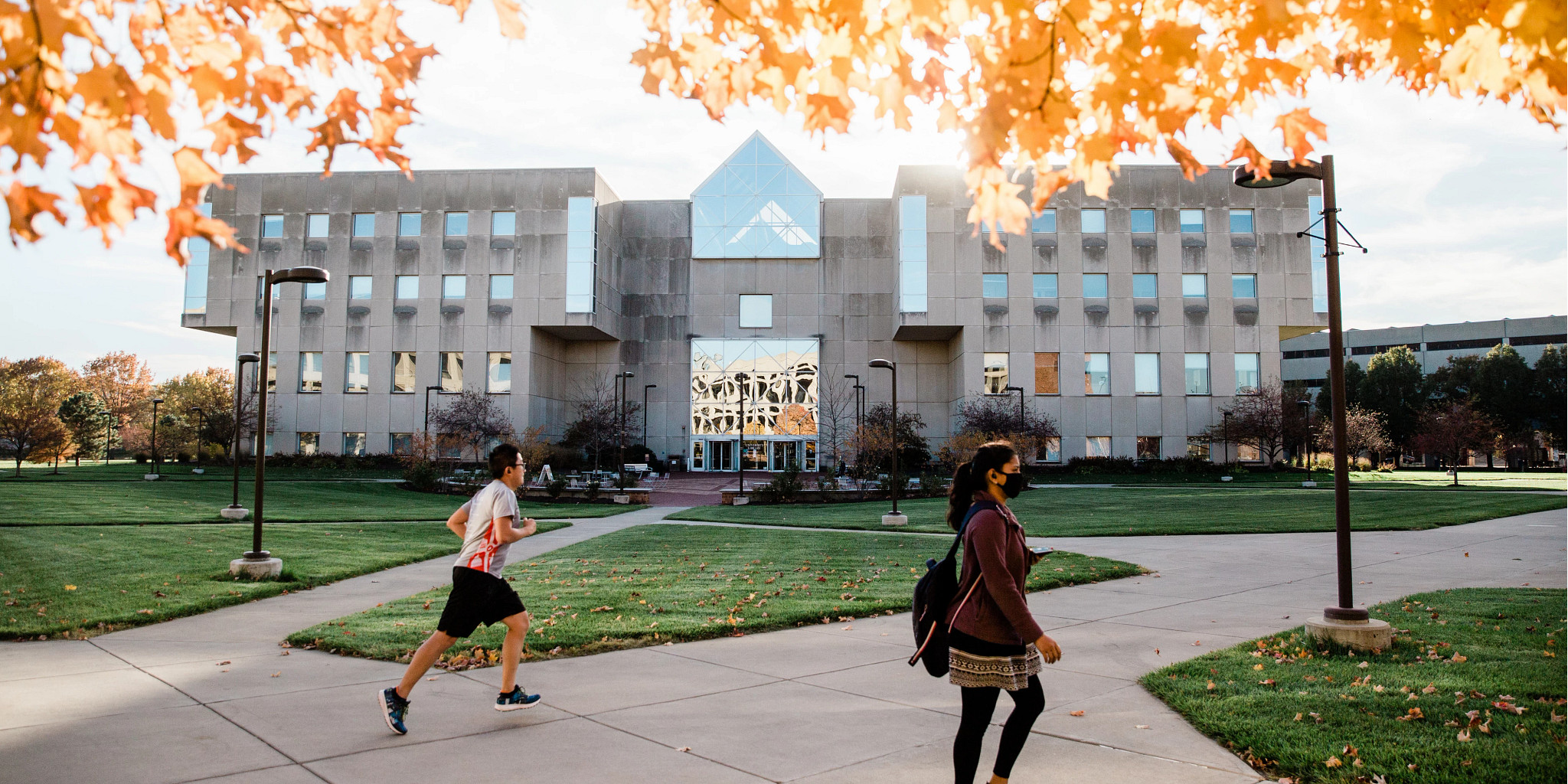 the fall trees frame University Library with two people passing by