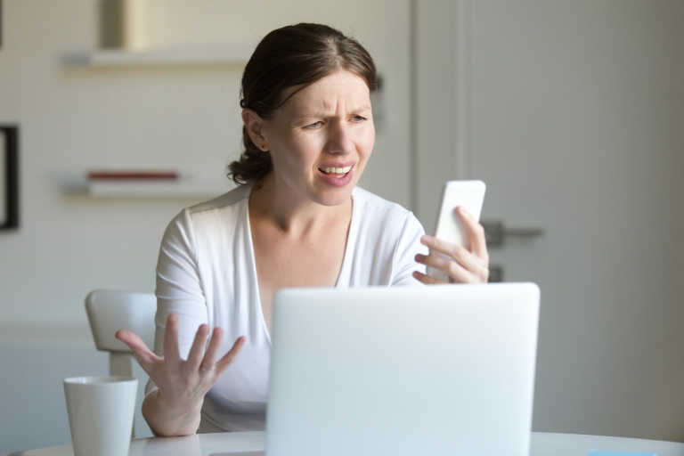 A woman looks in disgust at a cell phone in her hand