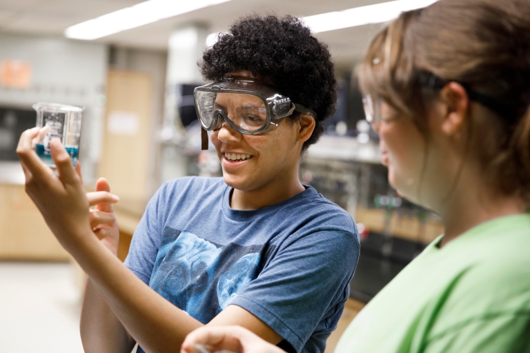 Student in a science lab holding a beaker with blue liquid