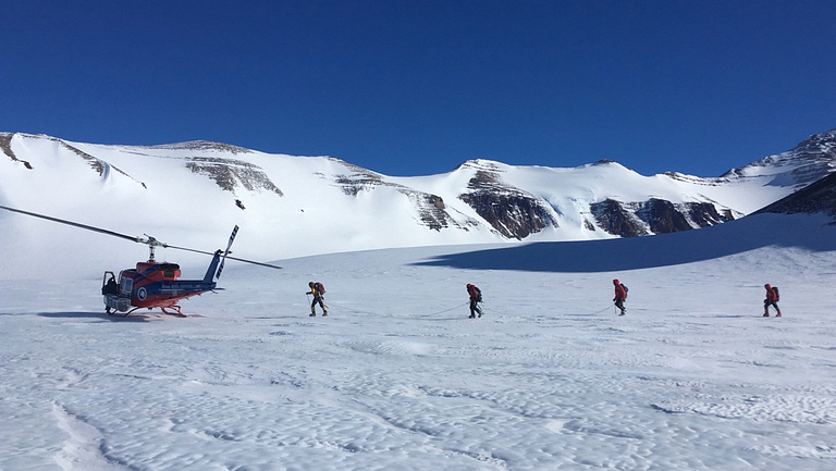 Researchers walk to a helicopter in Antarctica.