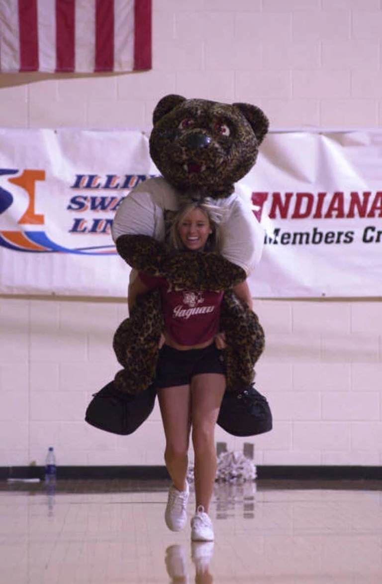 a cheerleader carries jinx the mascot on her back