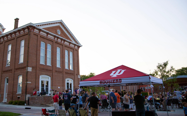 People gather outdoors around a small tent that displays the IU logo.