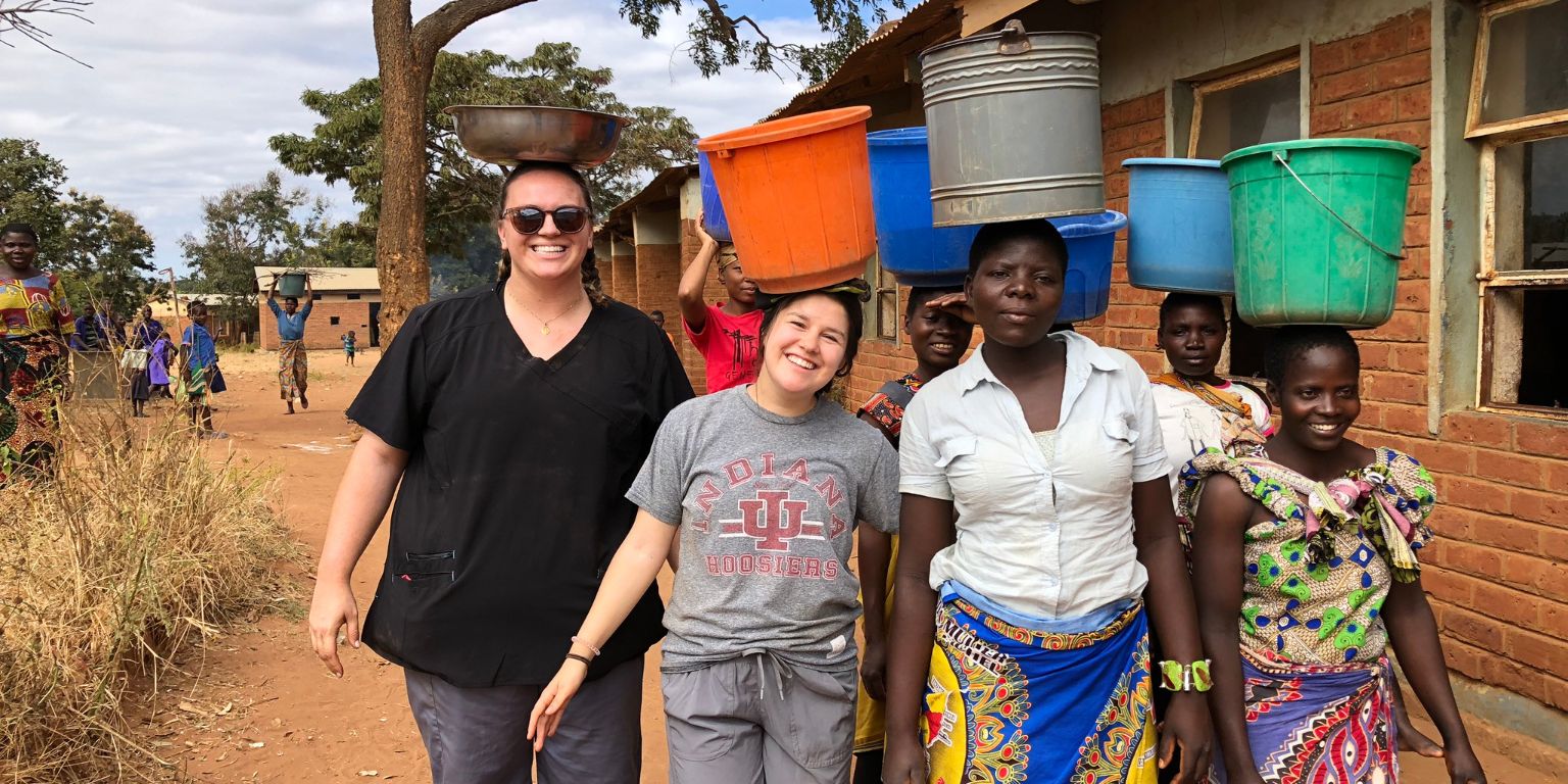 Seven women carry buckets on their heads