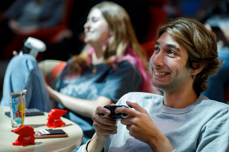 A student smiles and holds an Xbox controller while he plays.