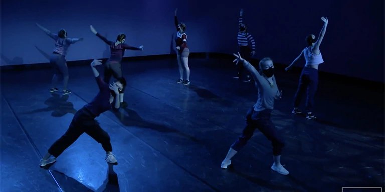 Dancers in two lines pose with their arms extended in dark blue light.
