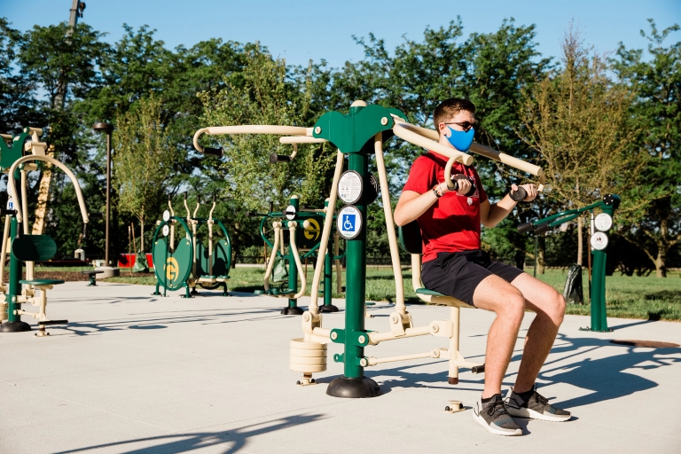 A person wearing a mask uses fitness equipment outdoors.