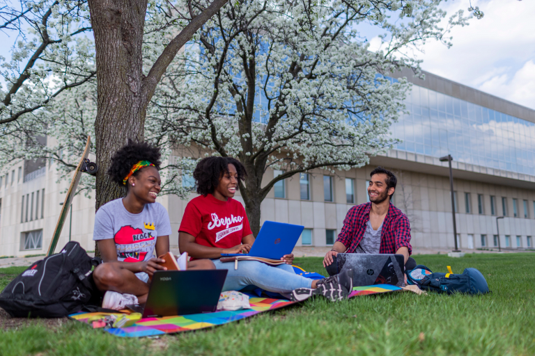 Students sit under a tree with their laptops on the IUPUI campus