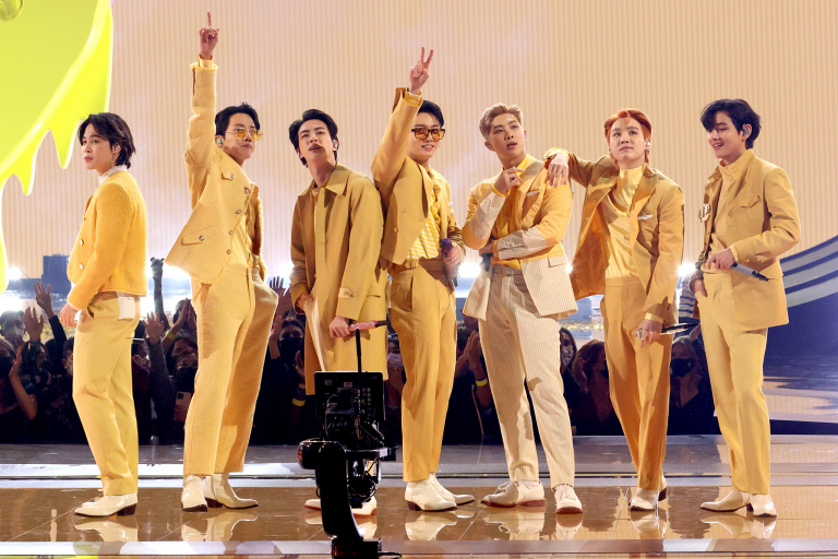 A group of Korean pop singers pose onstage in matching yellow suits at the American Music Awards.