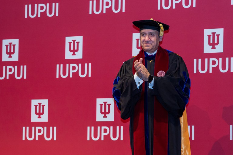 Chancellor Nasser H. Paydar wearing a cap and gown standing in front of an IUPUI backdrop
