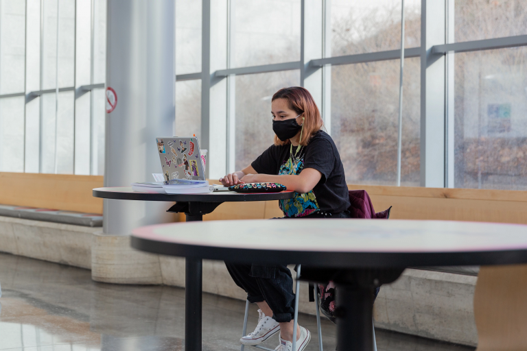 A student wearing a mask works on a laptop
