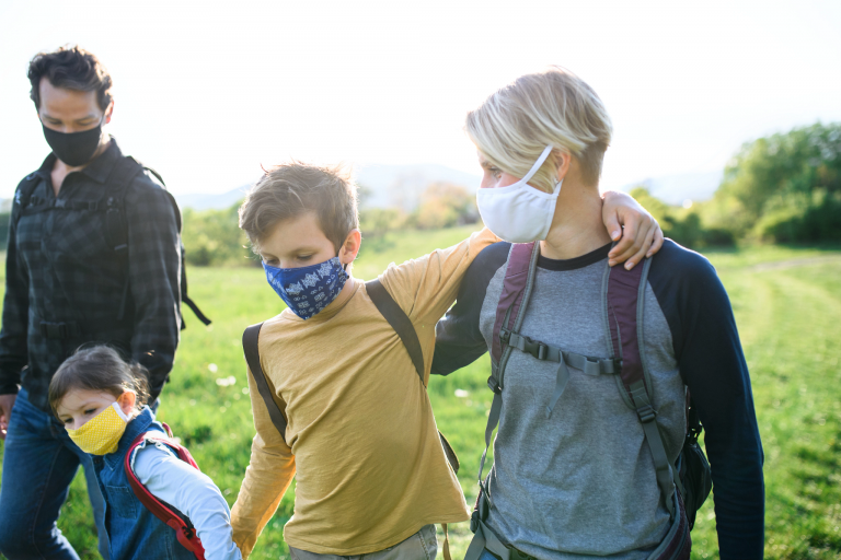 A family wearing face masks takes a walk in the countryside