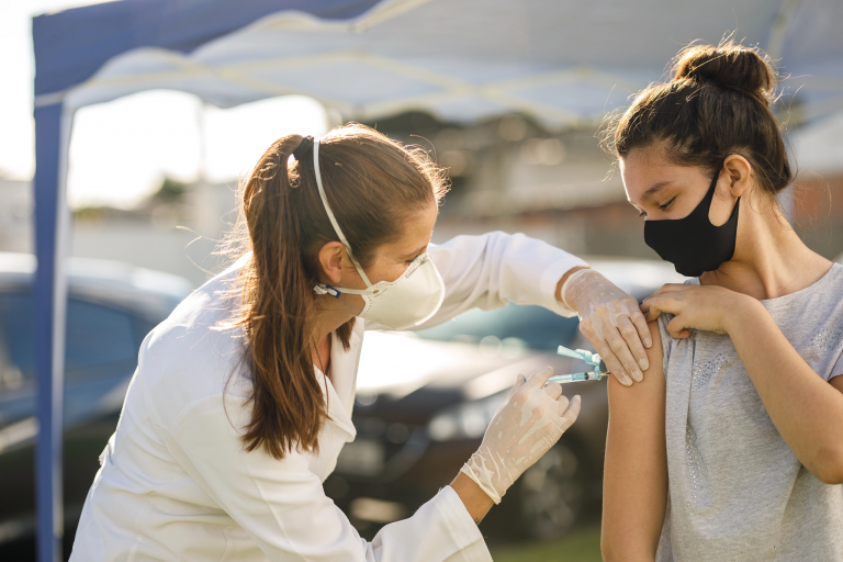 A teenager wearing a face mask gets a vaccine from a health care worker.