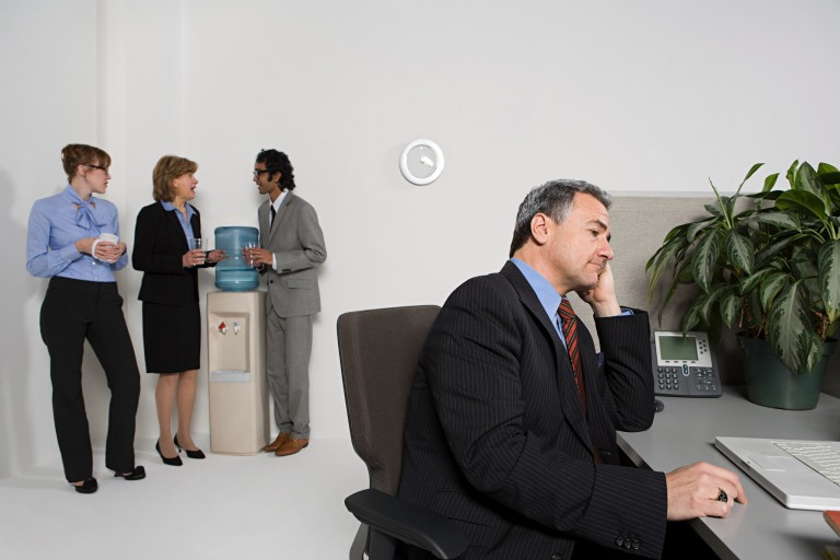 co-workers talk at the water cooler while a boss sits nearby