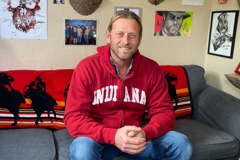 Rob Wiethoff, actor behind John Marston, sits on his couch wearing an IU sweatshirt