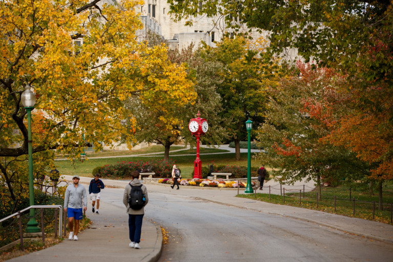 Students walk near a red clock on the IU Bloomington campus, surrounded by fall colors