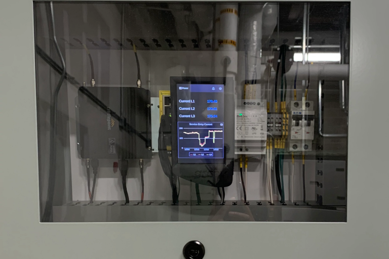 An energy monitor inside a gray metal box with a glass front