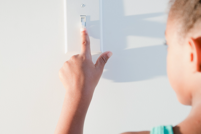 Young black girl turns on the light with a wall switch